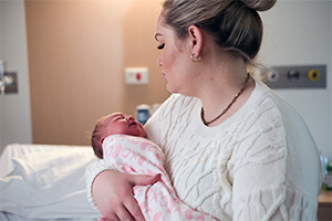 A woman sitting on a hospital bed holds a newborn baby.