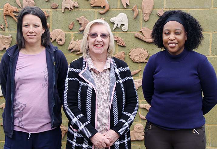 Three women standing in front of a feature wall.