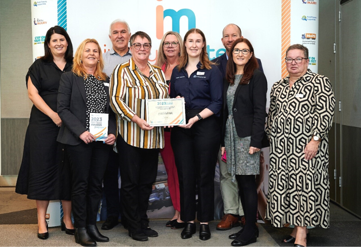 Nine members of the SMHS Health Promotion team standing together smiling, with two holding the award certificate in the middle.