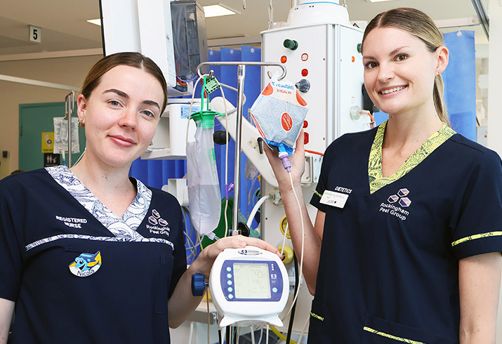 Two female intensive care unit nurses stand beside a a total closed-loop enteral feeding system