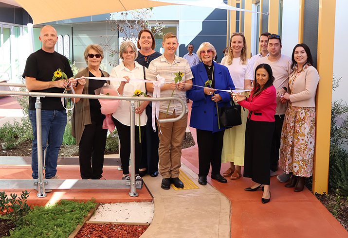 A dozen men and women stand together in an outdoor area designed to support rehabilitation in aged care patients