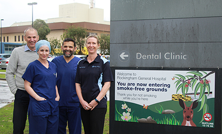 Four hospital staff stand in front of signage that reads "Welcome to Rockingham General Hospital. You are now entering smoke-free grounds. Thank you for not smoking while you are here."